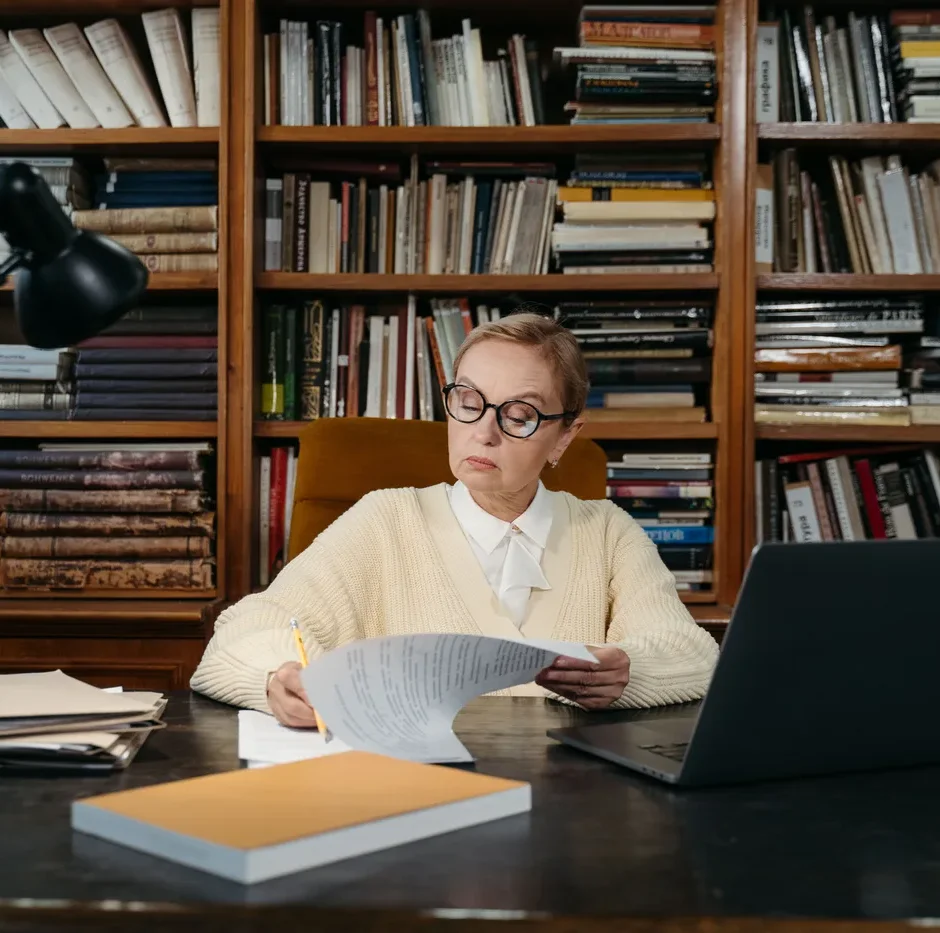 Senior academic consultant reviewing a manuscript in a library office